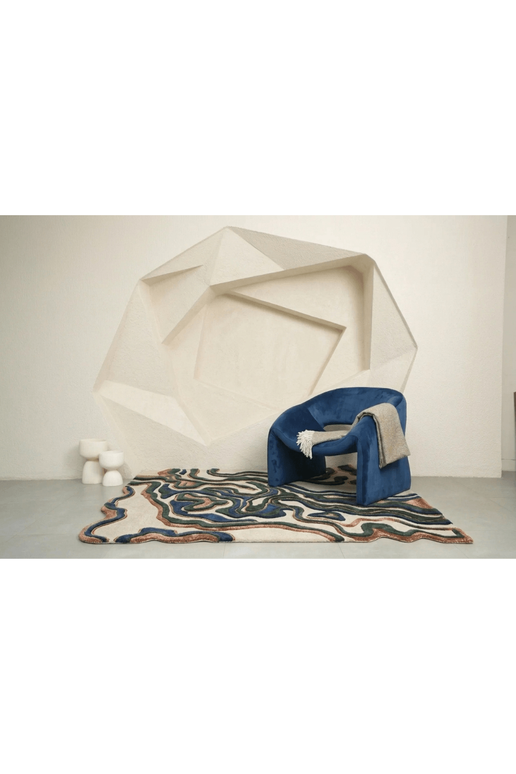 Terra Wave Contour Rug paired with blue chair against a geometric backdrop, showcasing organic curves and earthy tones.