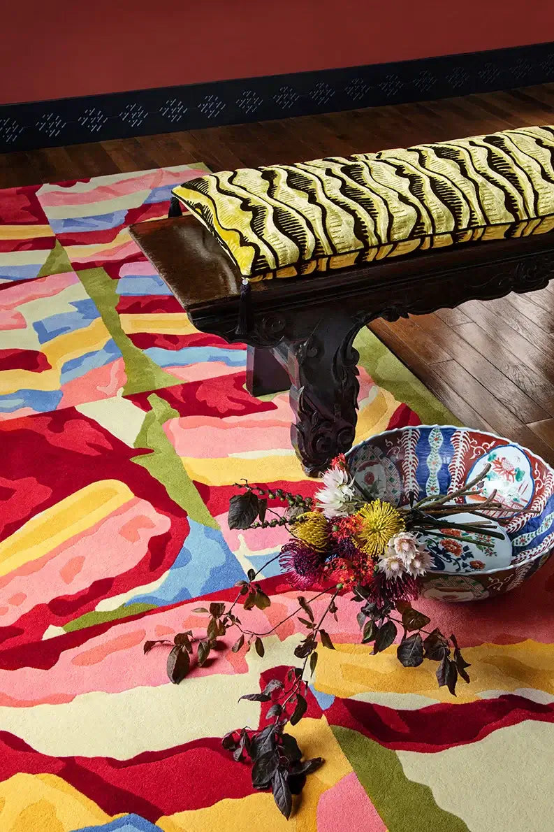 Vibrant Saekdong Reverie hand-tufted rug with colorful bands, alongside a decorative bowl and a wooden bench.