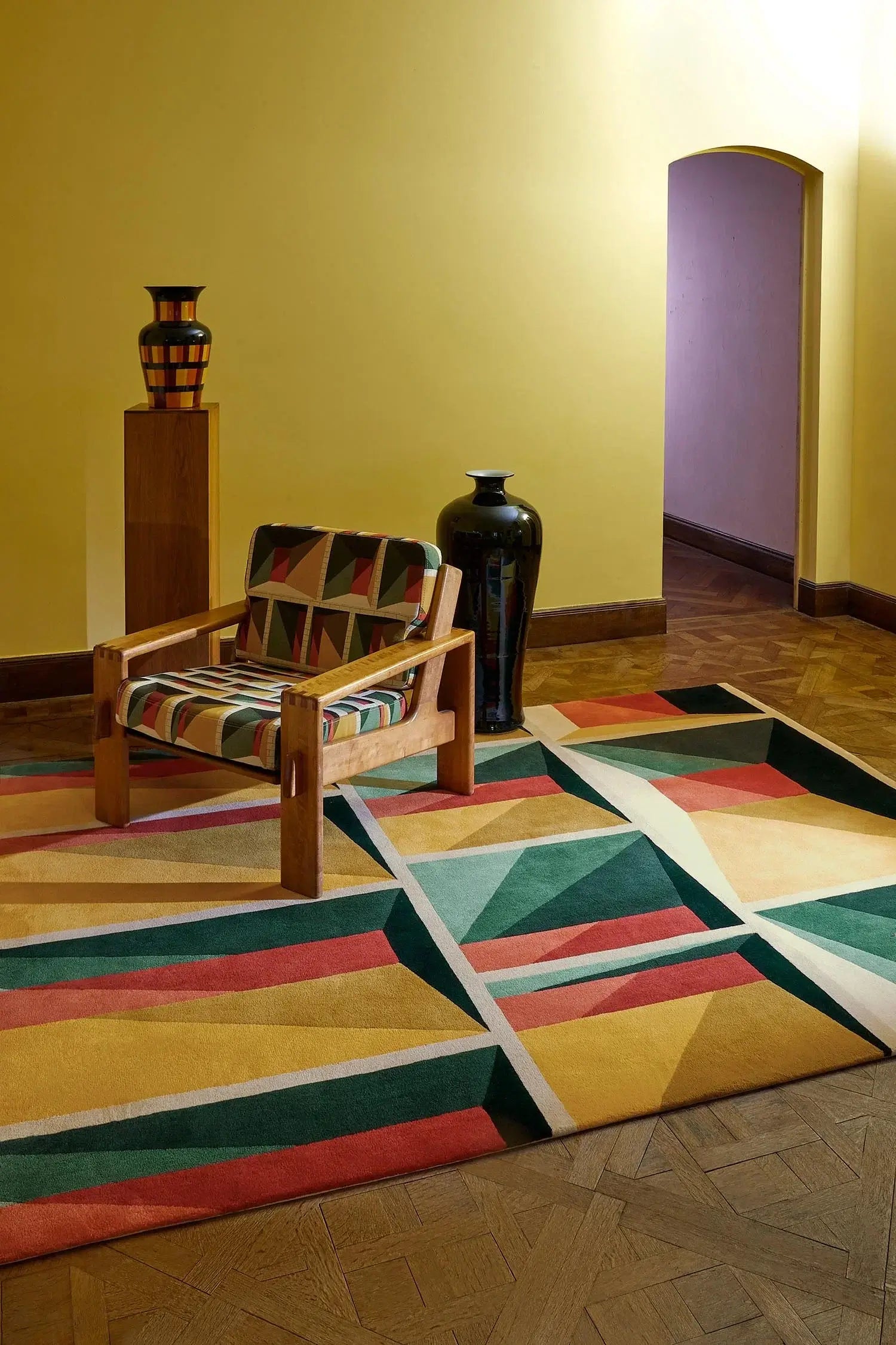 Facet Mirage Hand-Tufted Rug showcasing bold geometric patterns in vibrant colors against a yellow wall interior.