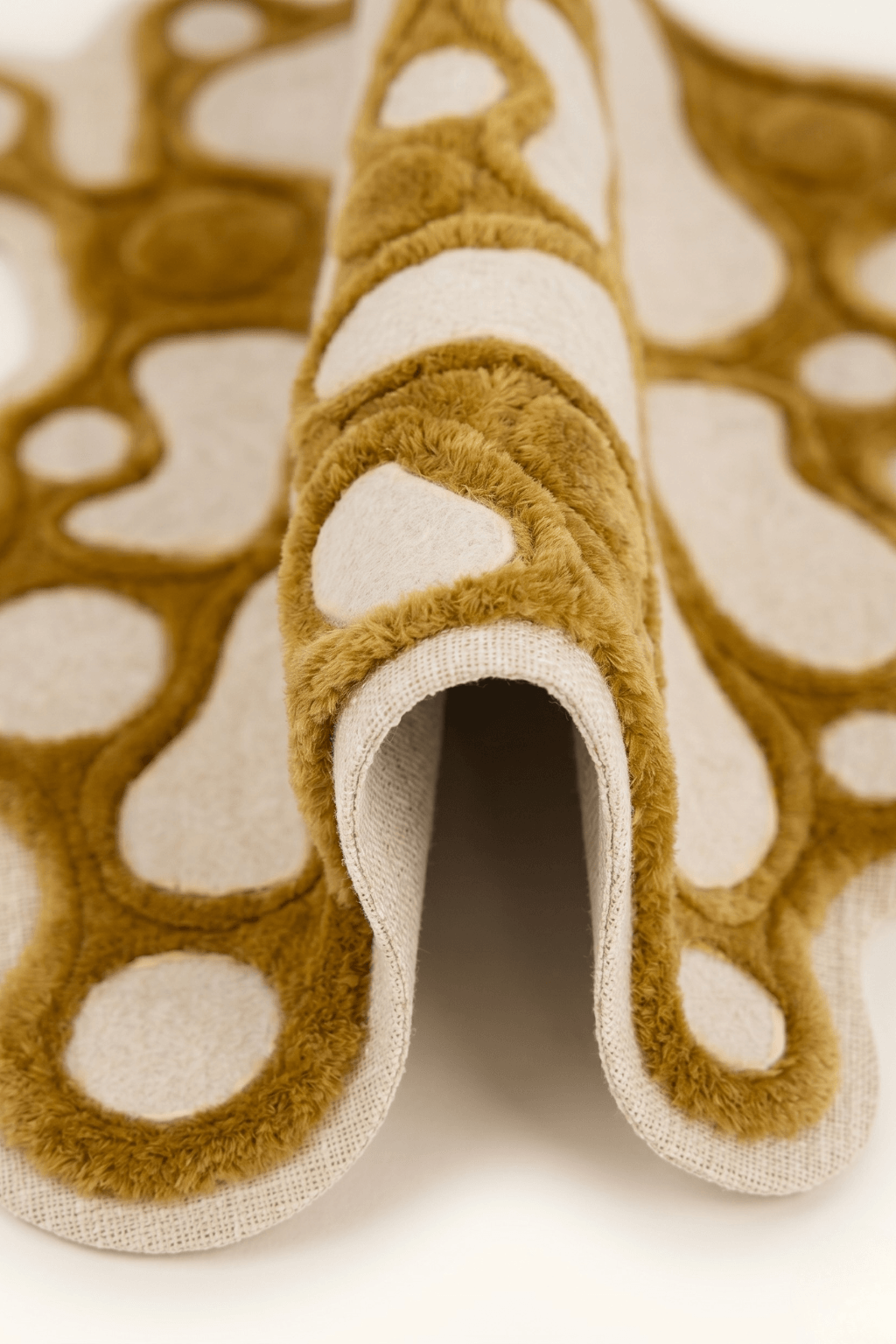 Close-up of artistic multi-texture rug, Amorphous Ochre, showcasing unique patterns and plush mustard-gold texture.