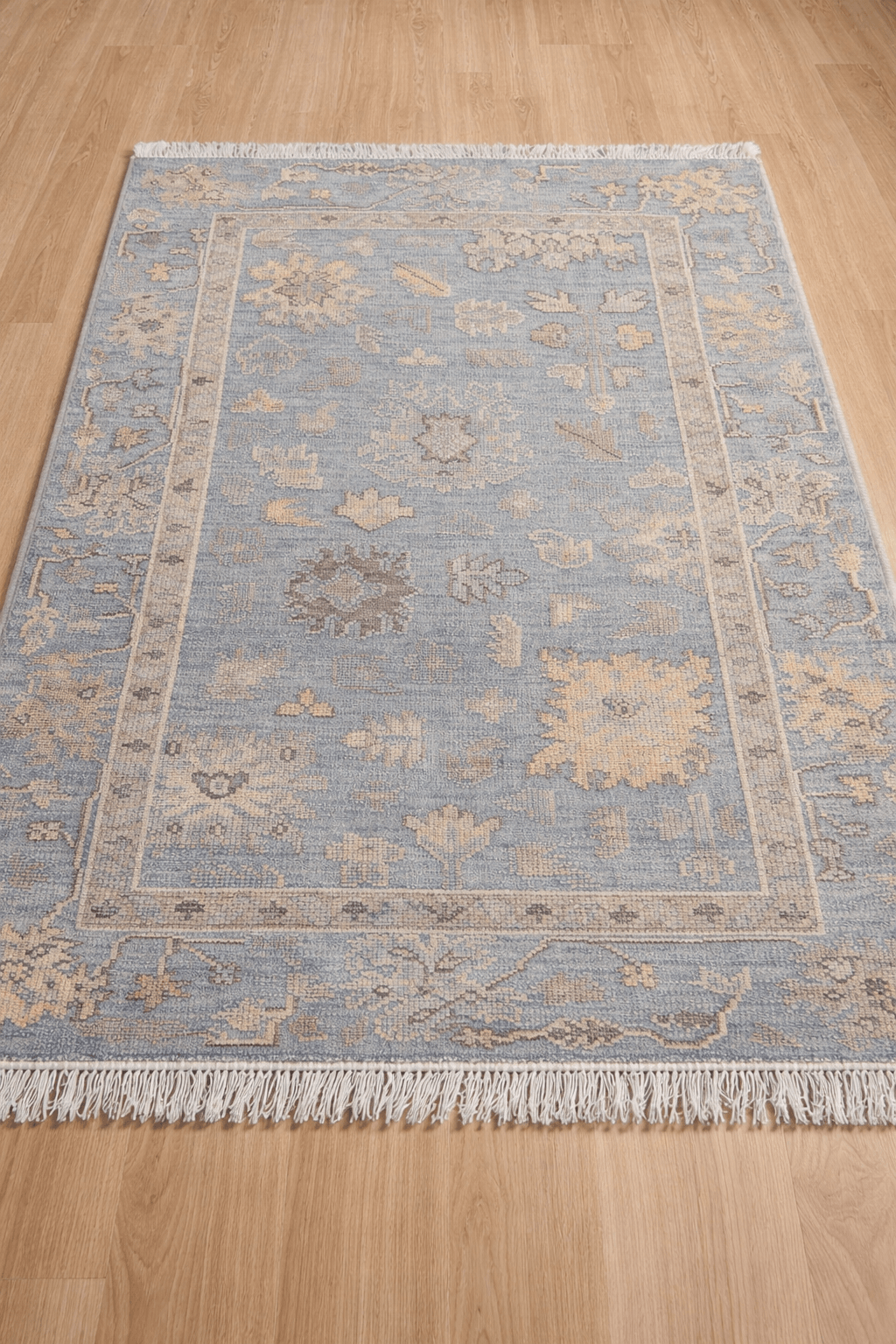 Dusty blue artisan hand-knotted rug with floral and geometric motifs on a wood floor.